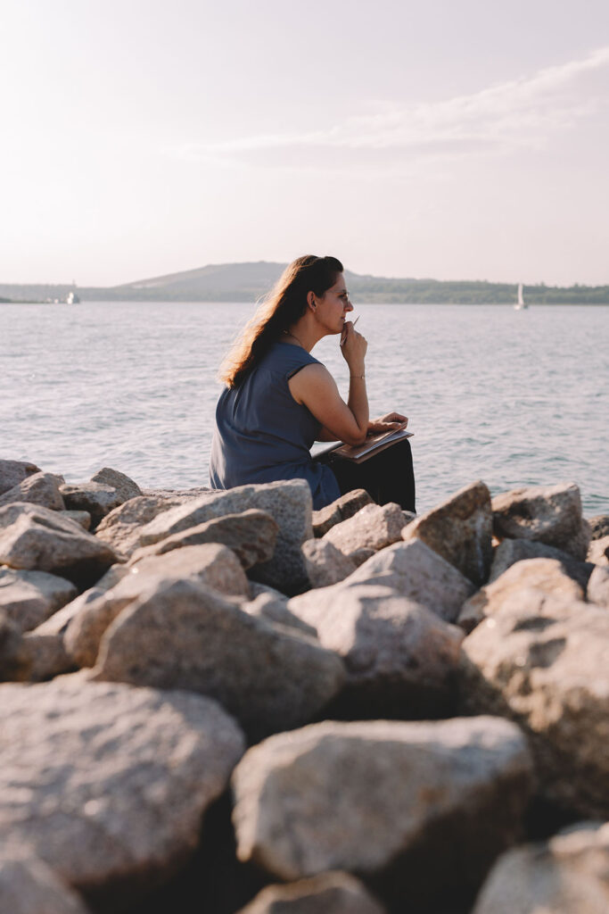 Frau sitzt auf Steinen und blickt aufs Wasser - Personal Branding Fotografie